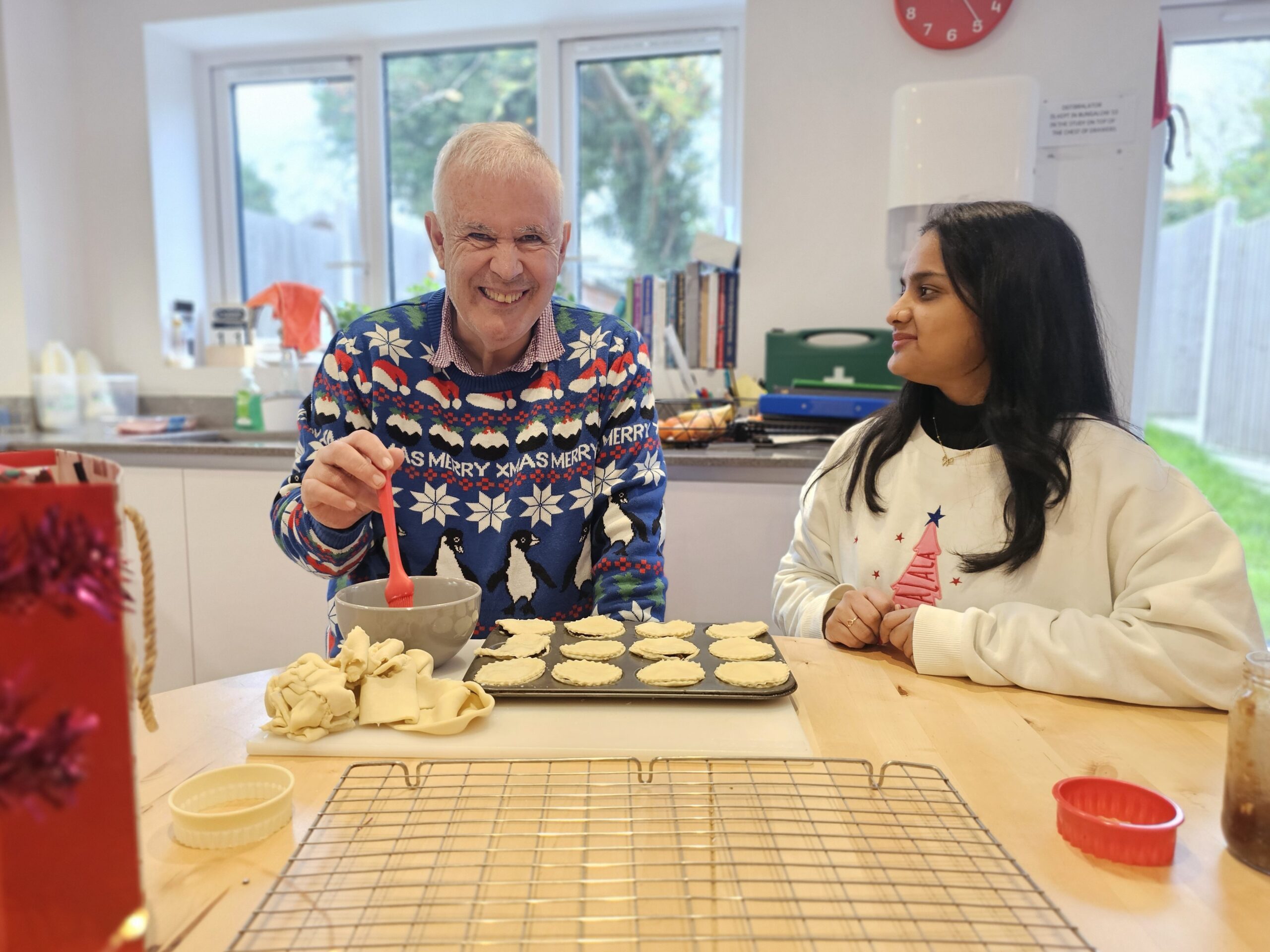 A man in a dark blue Christmas jumper, smiling for the camera, making mince pies with his Support Worker.