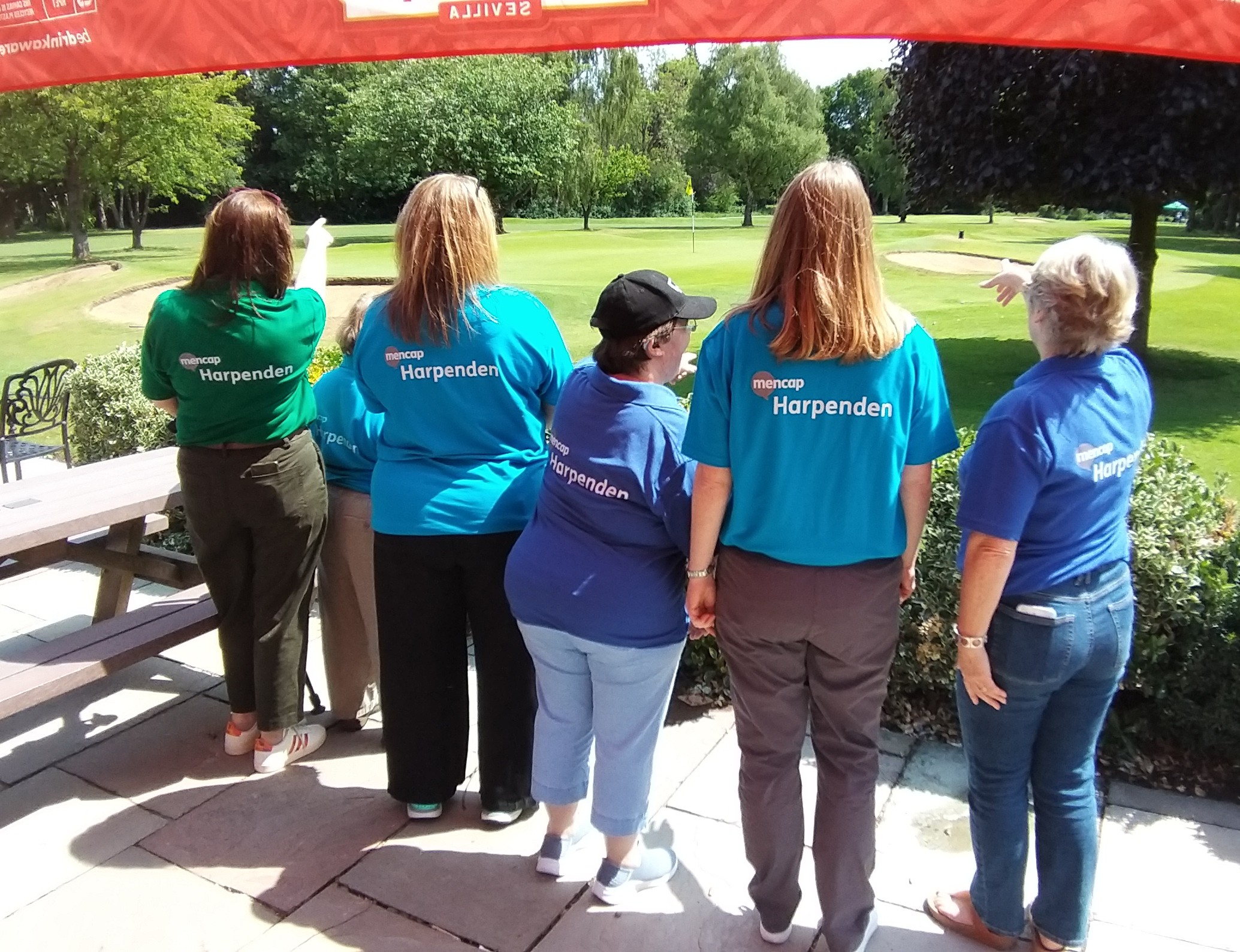 Harpenden Mencap team with their backs to the camera, displaying branded polo-shirts, looking out onto the green.