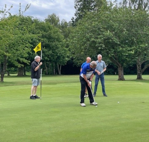Four men on the 18th, one standing with the flag, one putting, two more observing.