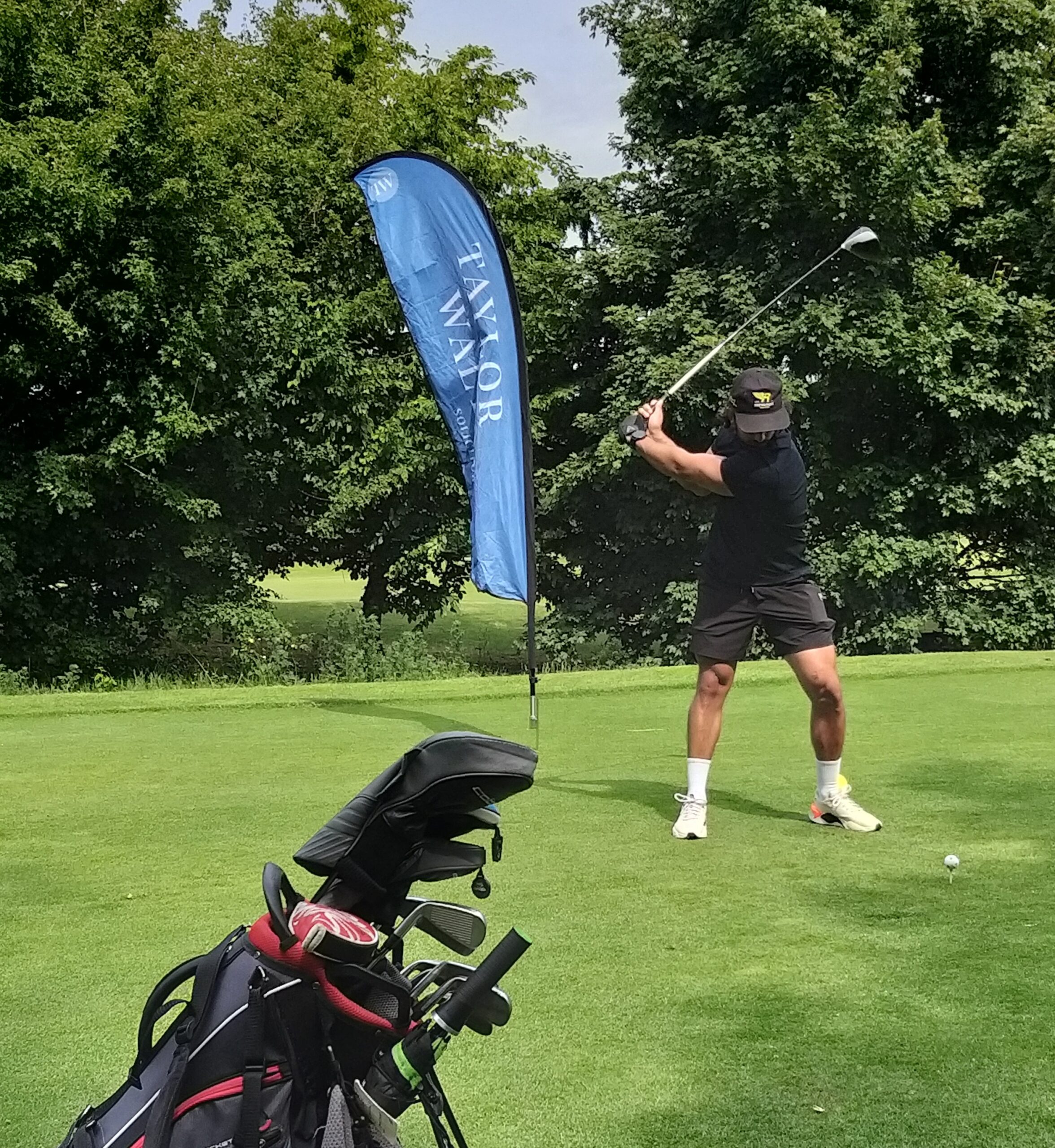 A man prepares to tee off beside a Taylor Walton flag.