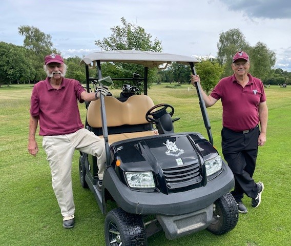 Two men wearing maroon polo shirts stand with a buggy.