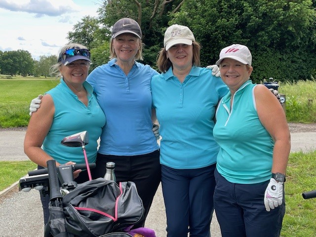 Four women wearing aqua-coloured polo shirts standing together and smiling for the camera.