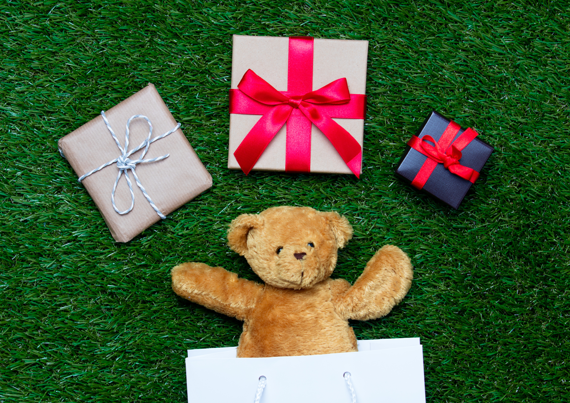 Wrapped raffle prizes arranged on Astroturf, including three square gifts with bows, a white gift bag, and a teddy bear.