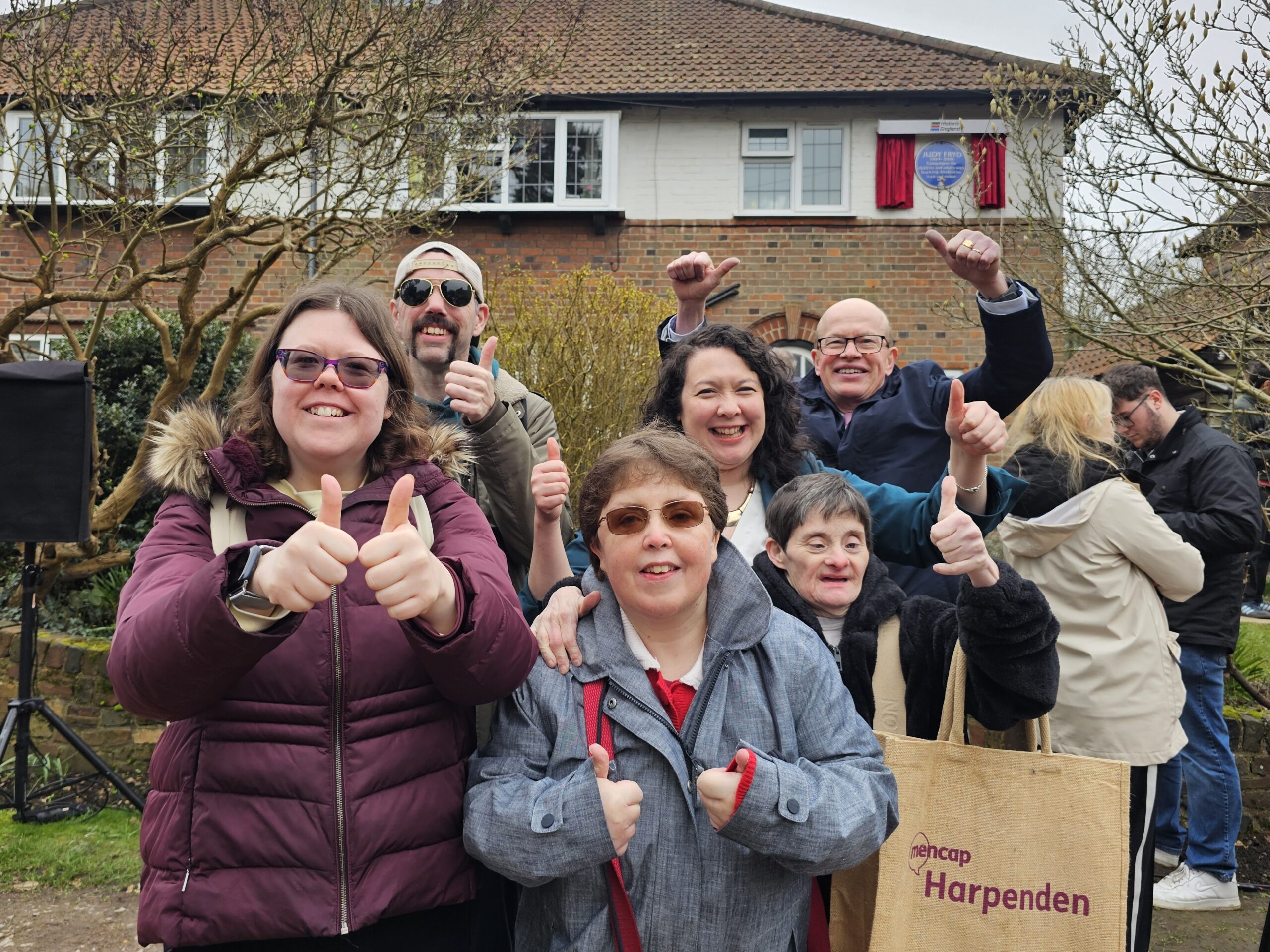 Harpenden Mencap community big smiles in front of the blue plaque - with Victoria Collins MP.